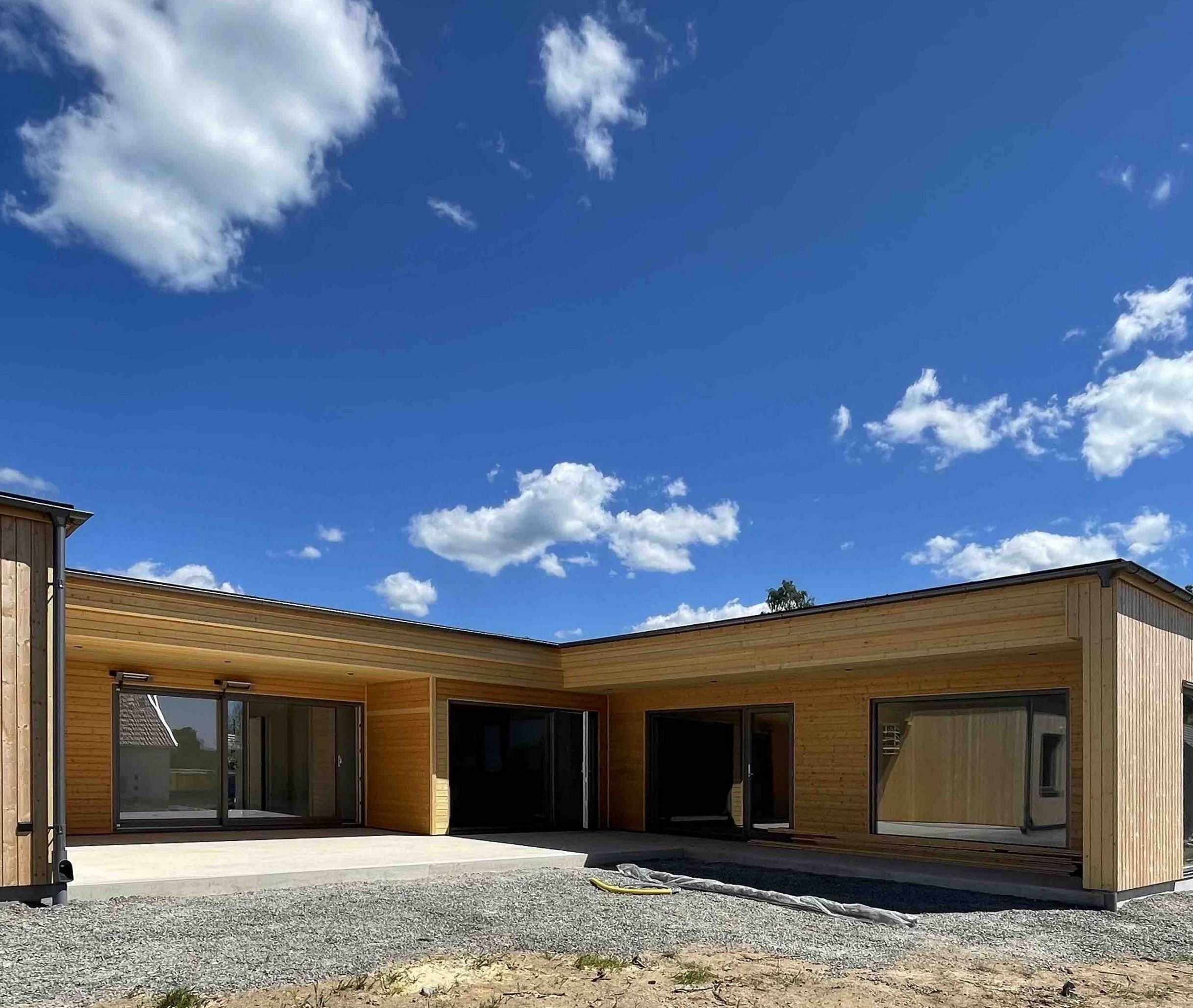 Nybyggt hus med liggande träpanel och stora glaspartier under blå himmel