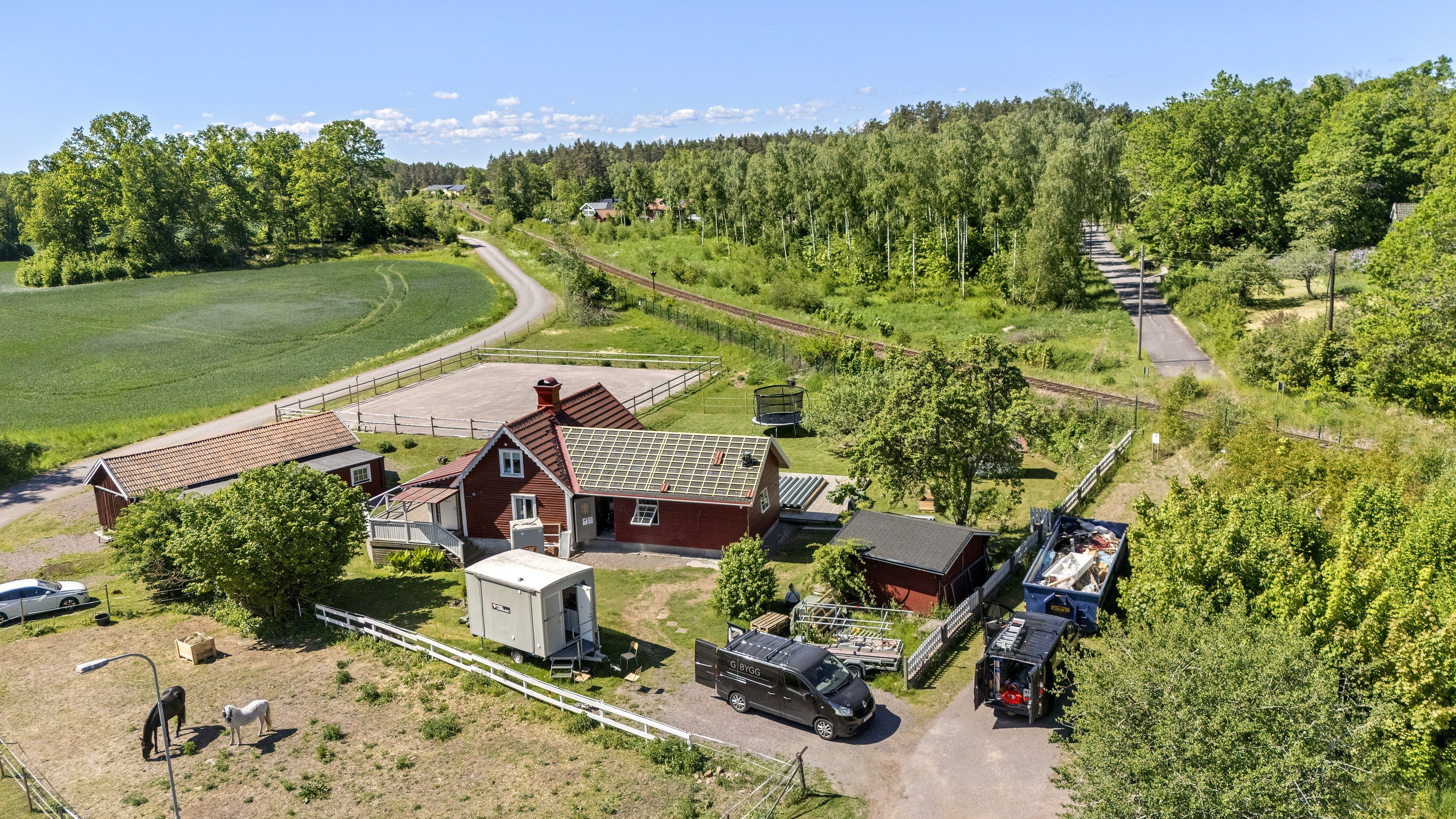 Flygfoto över en röd gård med uthus och grusad uppfart, omgiven av åker och skog