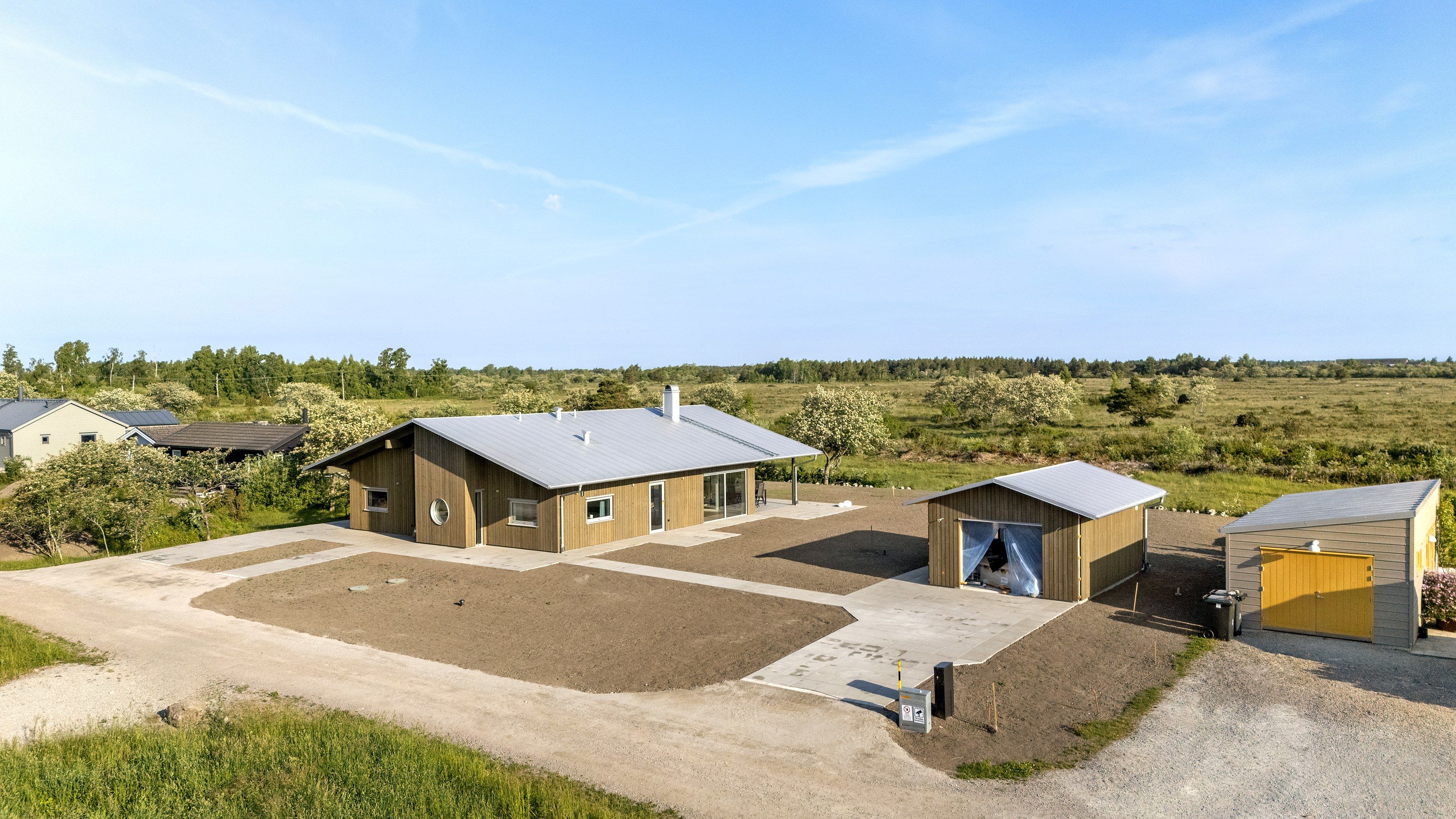 Nybyggt hus med garage och uthus på en öppen tomt under blå himmel