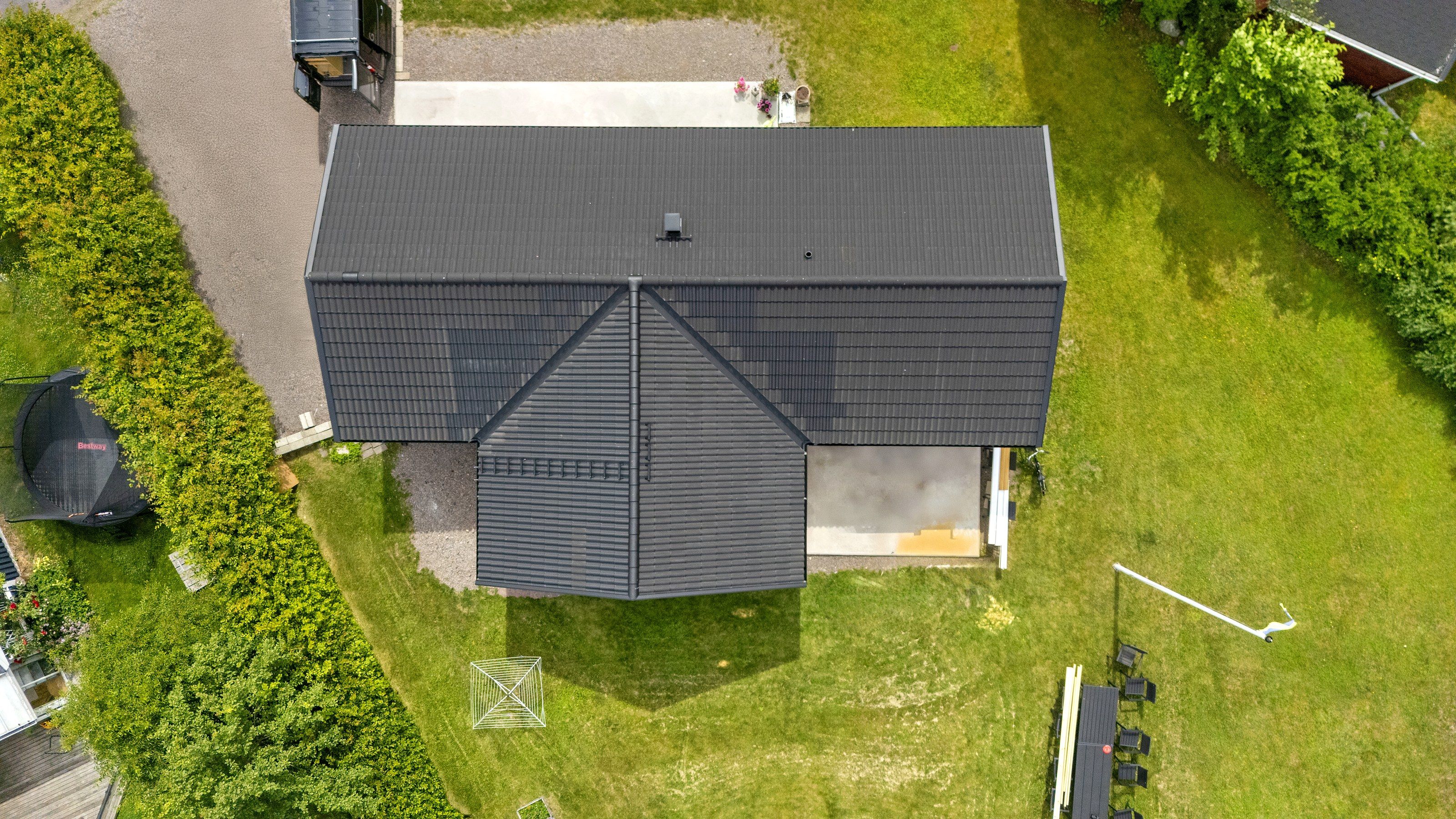 Flygfoto över ett hus med mörkt tak och en gräsmatta intill