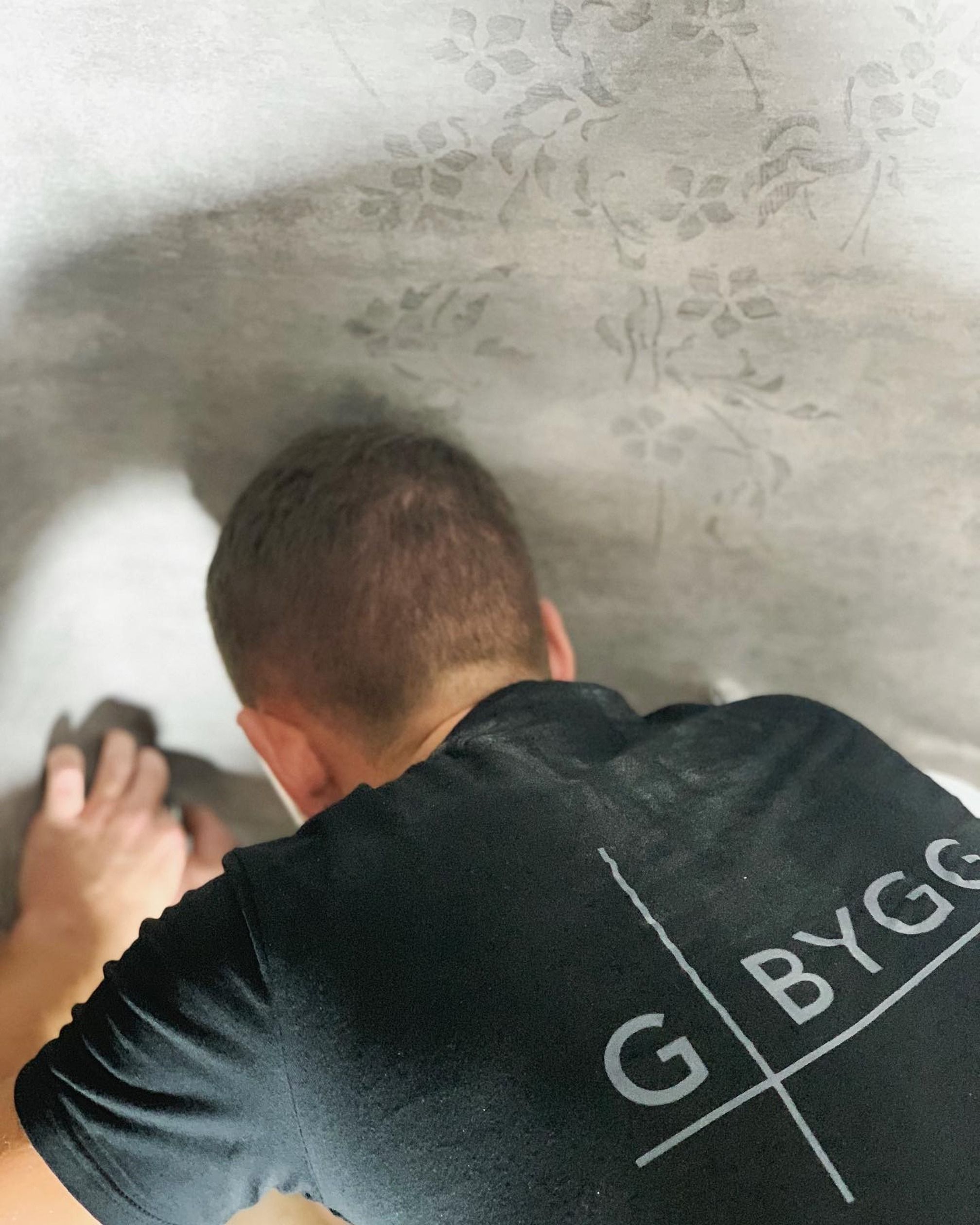 En medarbetare från G-Bygg i svart arbetströja jämnar till en grå microcementvägg med mönster
