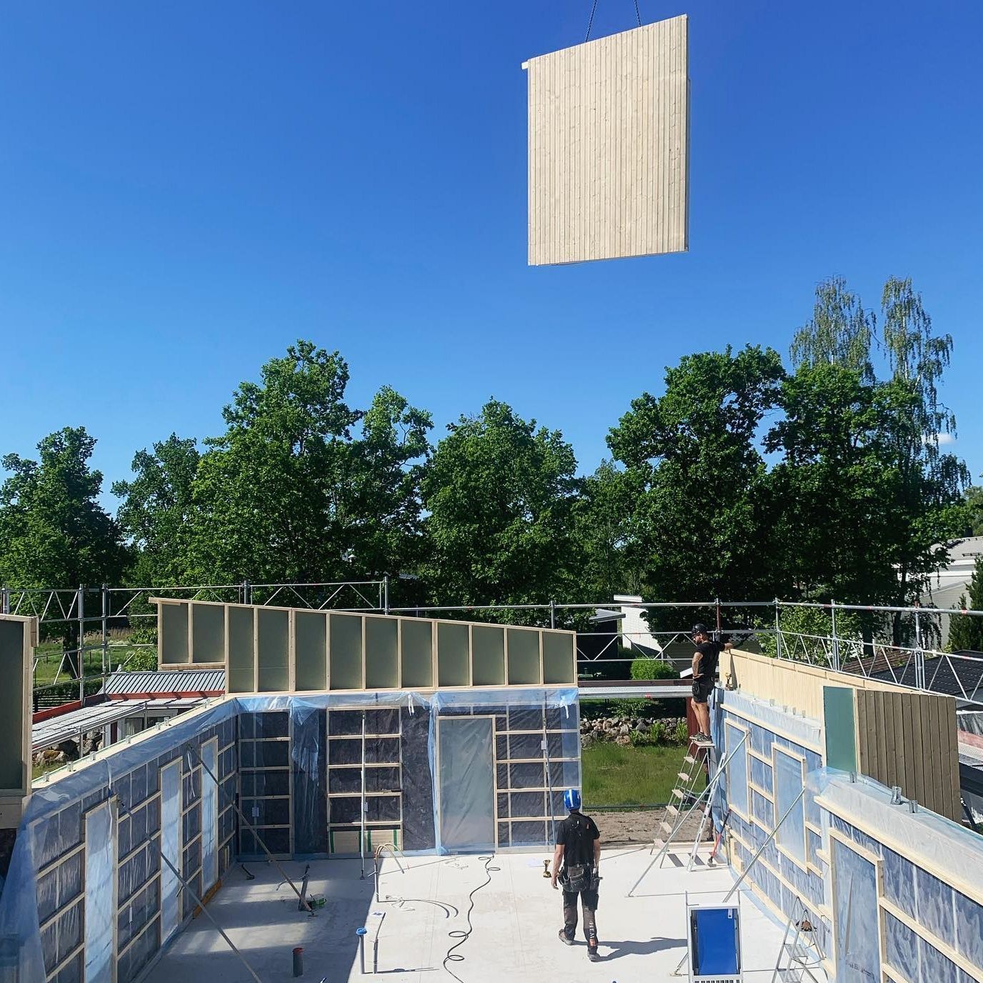 Ett väggelement lyfts på plats över ett hus under montering