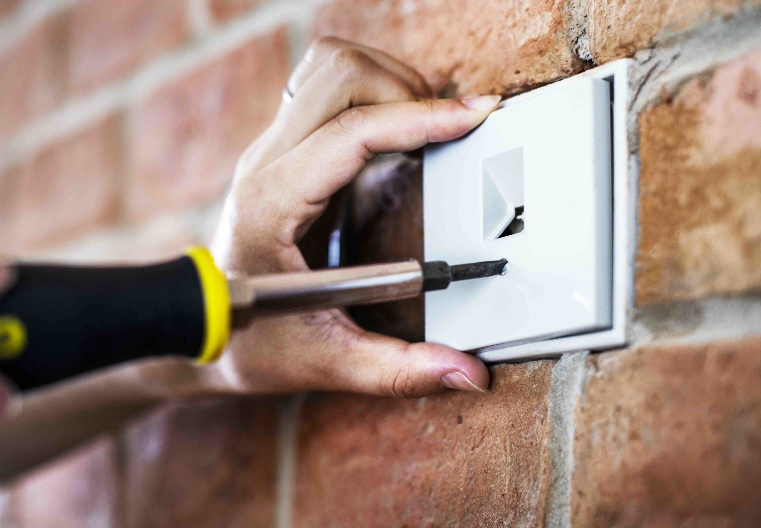 En elektriker monterar ett eluttag på en tegelvägg med skruvmejsel