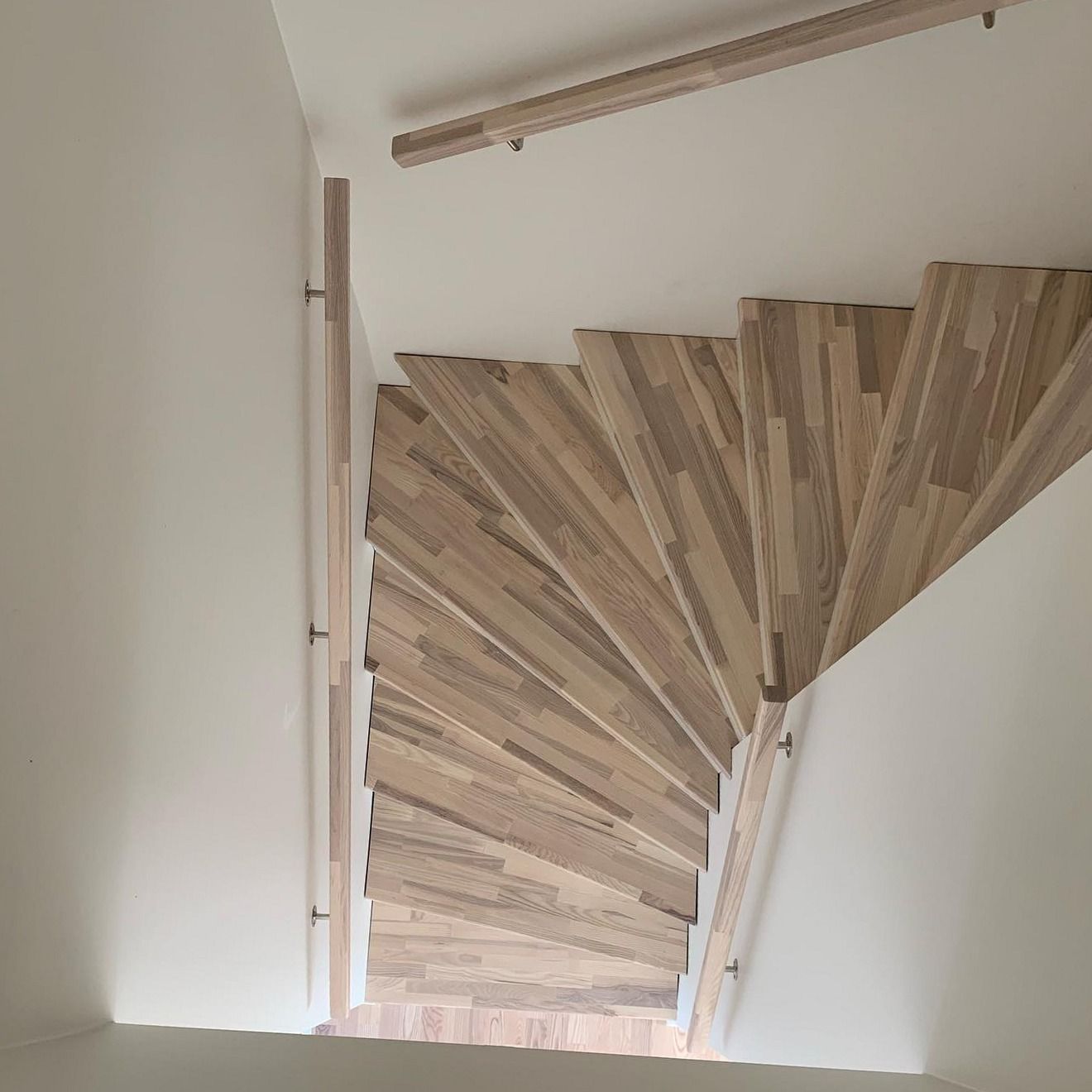 Trappa med ljusa trästeg och räcke sedd uppifrån i ett vitt trapphus